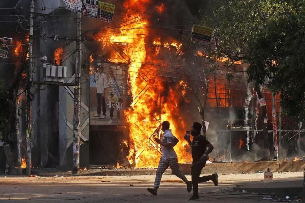 Homens passam correndo por um shopping que foi incendiado durante uma manifestação em  Bangladesh